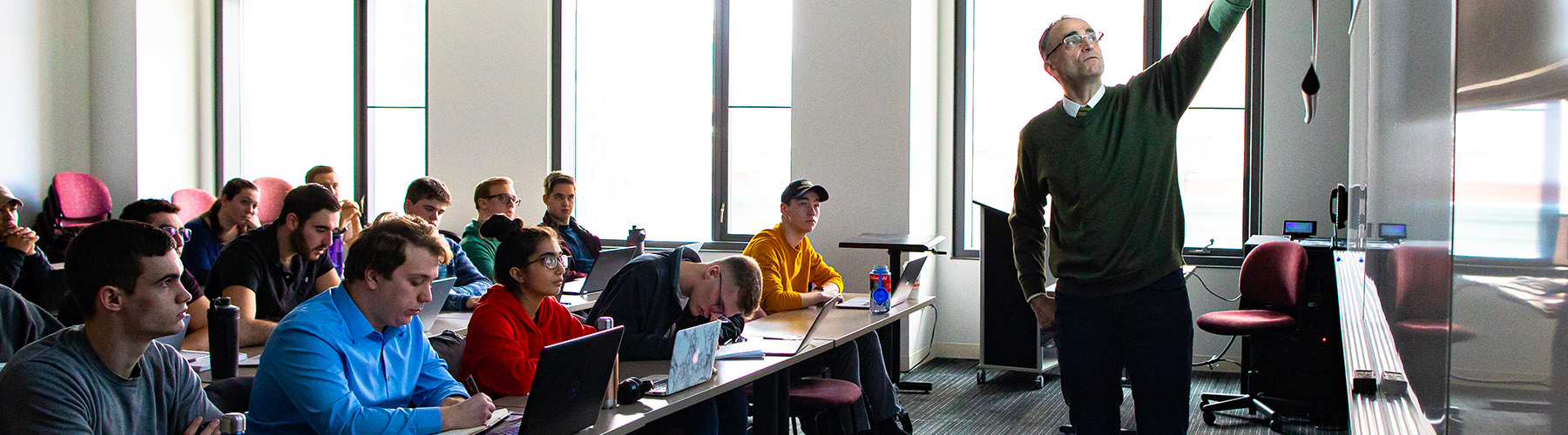 Engineering students work on their senior capstone projects in the Engineering Flex Lab as one student writes on a whiteboard.