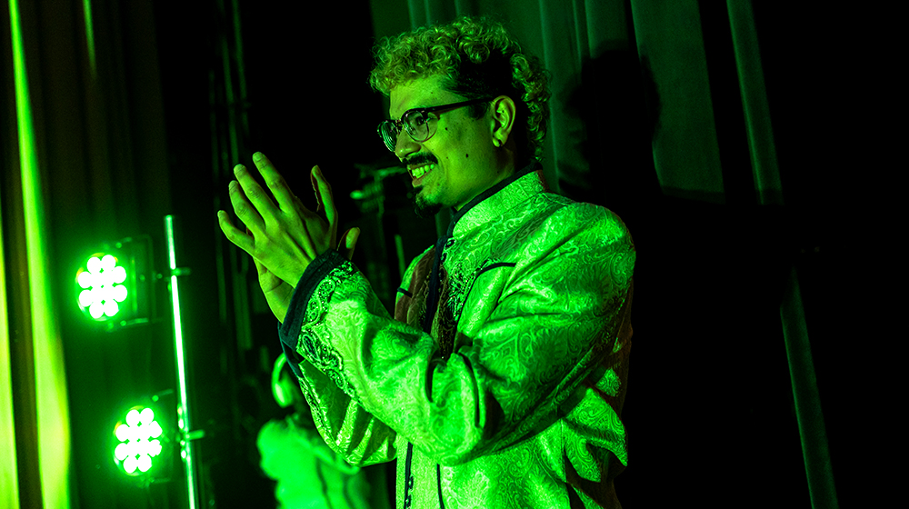 Joshua Zepeda (BA ’12, MSW ’15), stands and claps as he is awash in the green glow of the theater lighting.